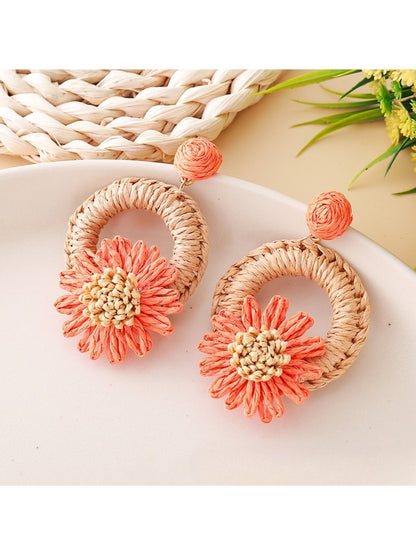 Earedge raffia daisy stud earrings placed next to green leaves for styling