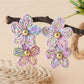 Earedge raffia drop earrings hanging on a wooden stand