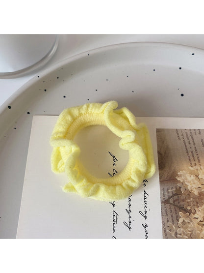 Multiple colorful ruffled hair ties spread out on a pastel background
