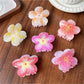 Beau floral claw clip held in hand showing translucent acetate material and detailed petals