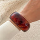 Lovra gold round bangle bracelet resting on a textured fabric background