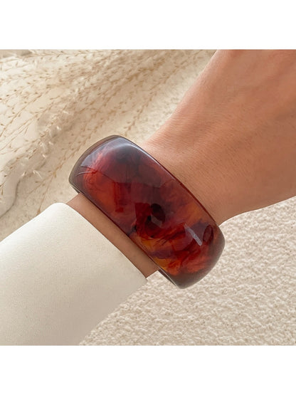 Lovra gold round bangle bracelet resting on a textured fabric background
