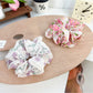 Gifty floral scrunchie worn on a wrist, showcasing ruffled design and bow accent