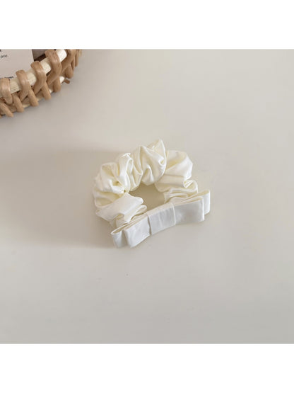 Model tying hair with the minimalist satin bow scrunchie in a low ponytail