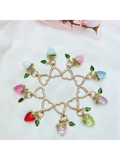 Keypus strawberry charm keychain hanging from a set of keys on wooden surface