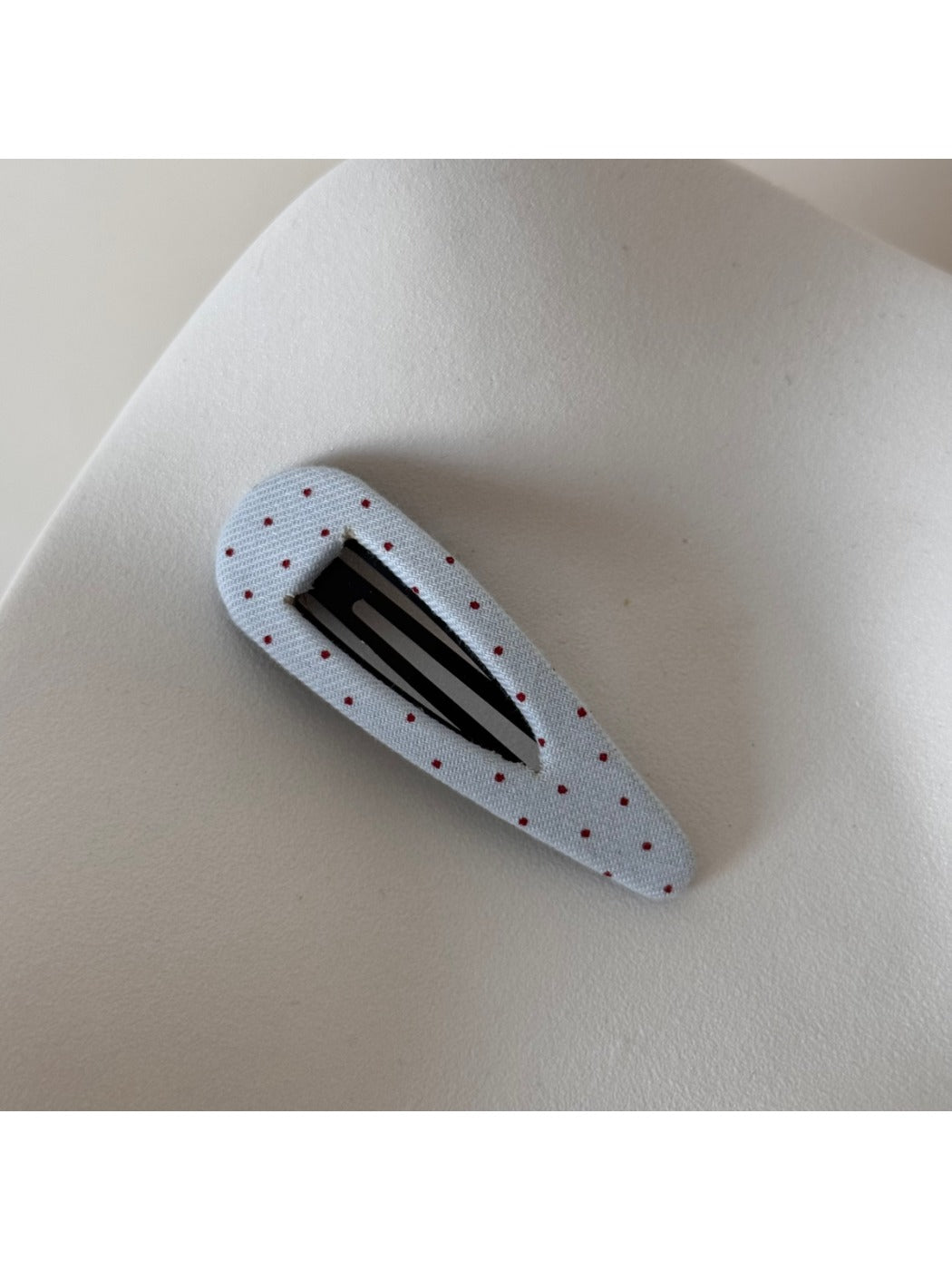 Beau hair clip with white polka dots on pink fabric background