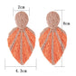 Earedge raffia woven leaf shaped earrings displayed on a wooden surface