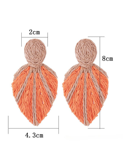 Earedge raffia woven leaf shaped earrings displayed on a wooden surface