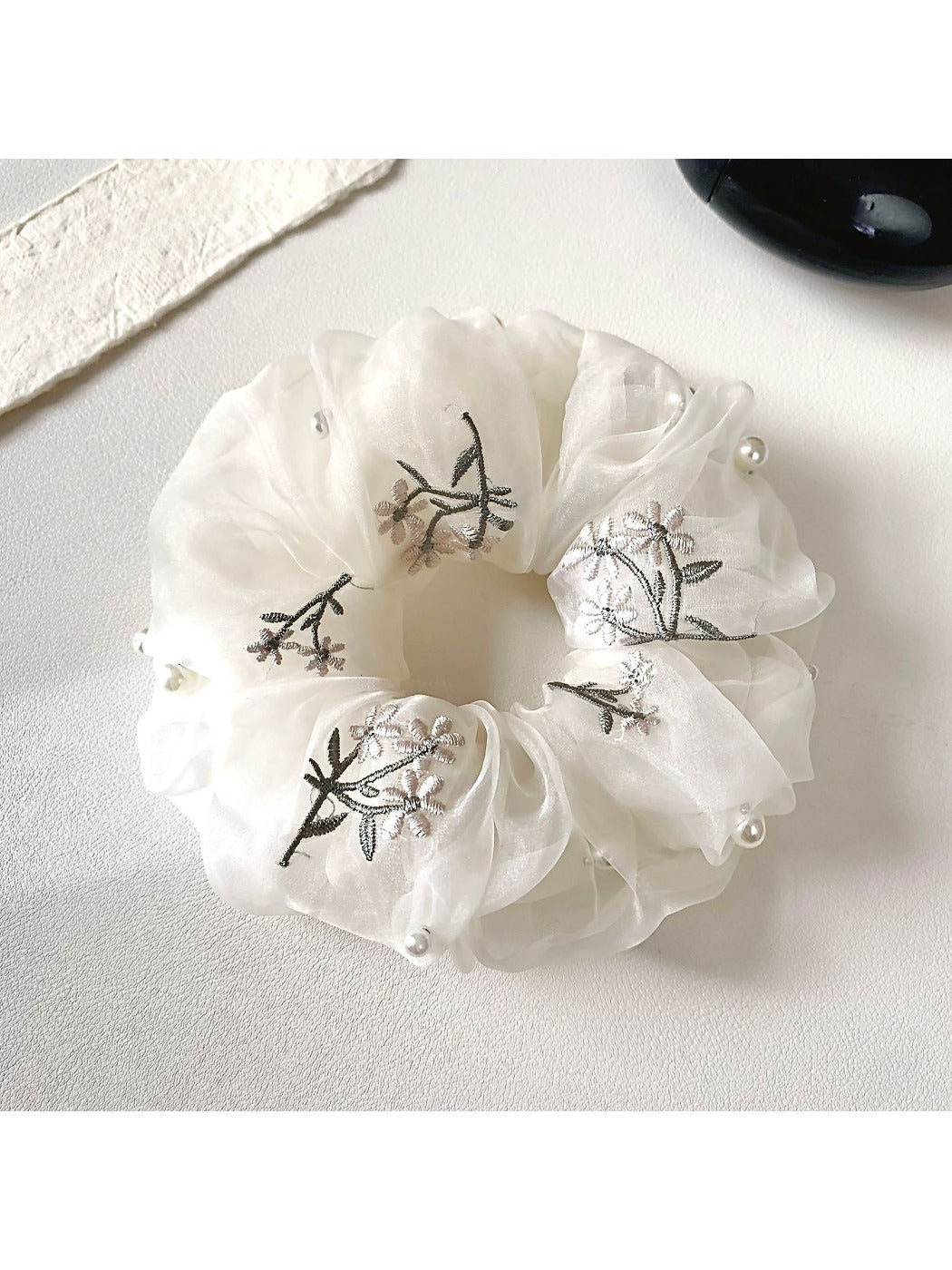 Close-up of a dainty white floral scrunchie with delicate flower patterns on fabric