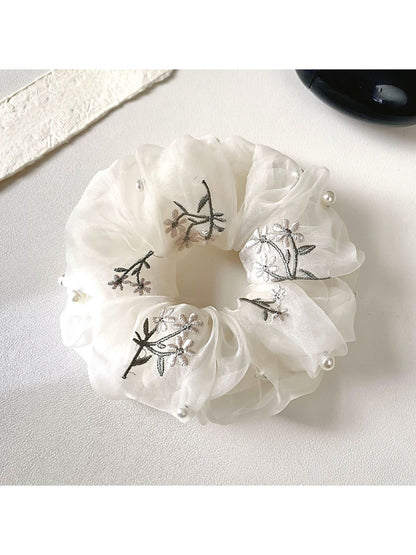 Close-up of a dainty white floral scrunchie with delicate flower patterns on fabric