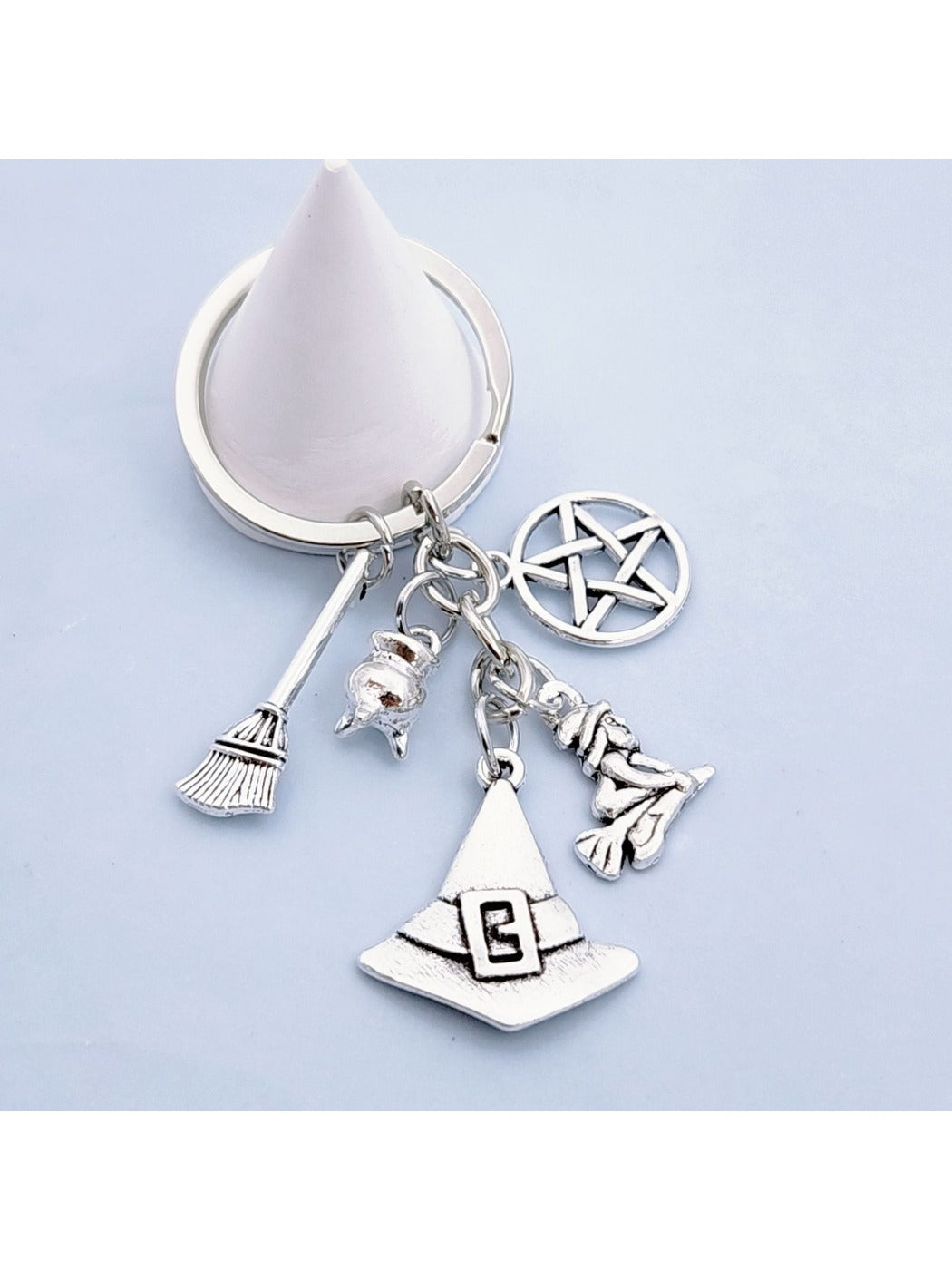 Silver alloy witch hat keychain with broom charm on a wooden surface