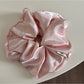 Glossy satin scrunchie in soft pink wrapped around a ponytail