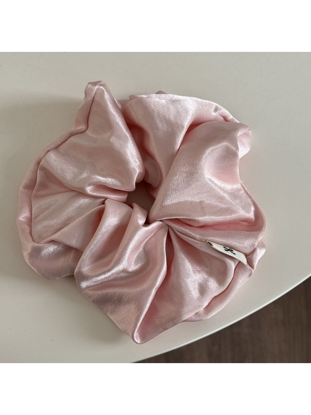 Glossy satin scrunchie in soft pink wrapped around a ponytail