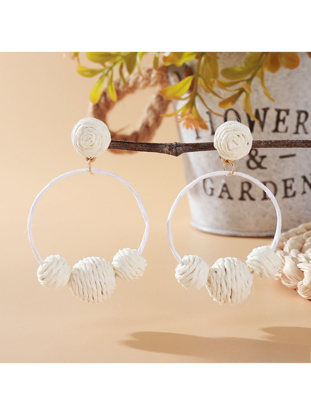 Pair of Earedge raffia round ball earrings on a wooden surface