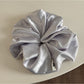 Glossy satin scrunchie in pink with light reflecting off smooth fabric