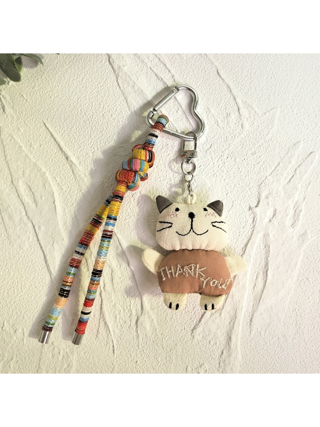 Cat charm keychain hanging from a backpack zipper in outdoor setting