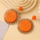 Earedge raffia round earrings placed next to green leaves for styling