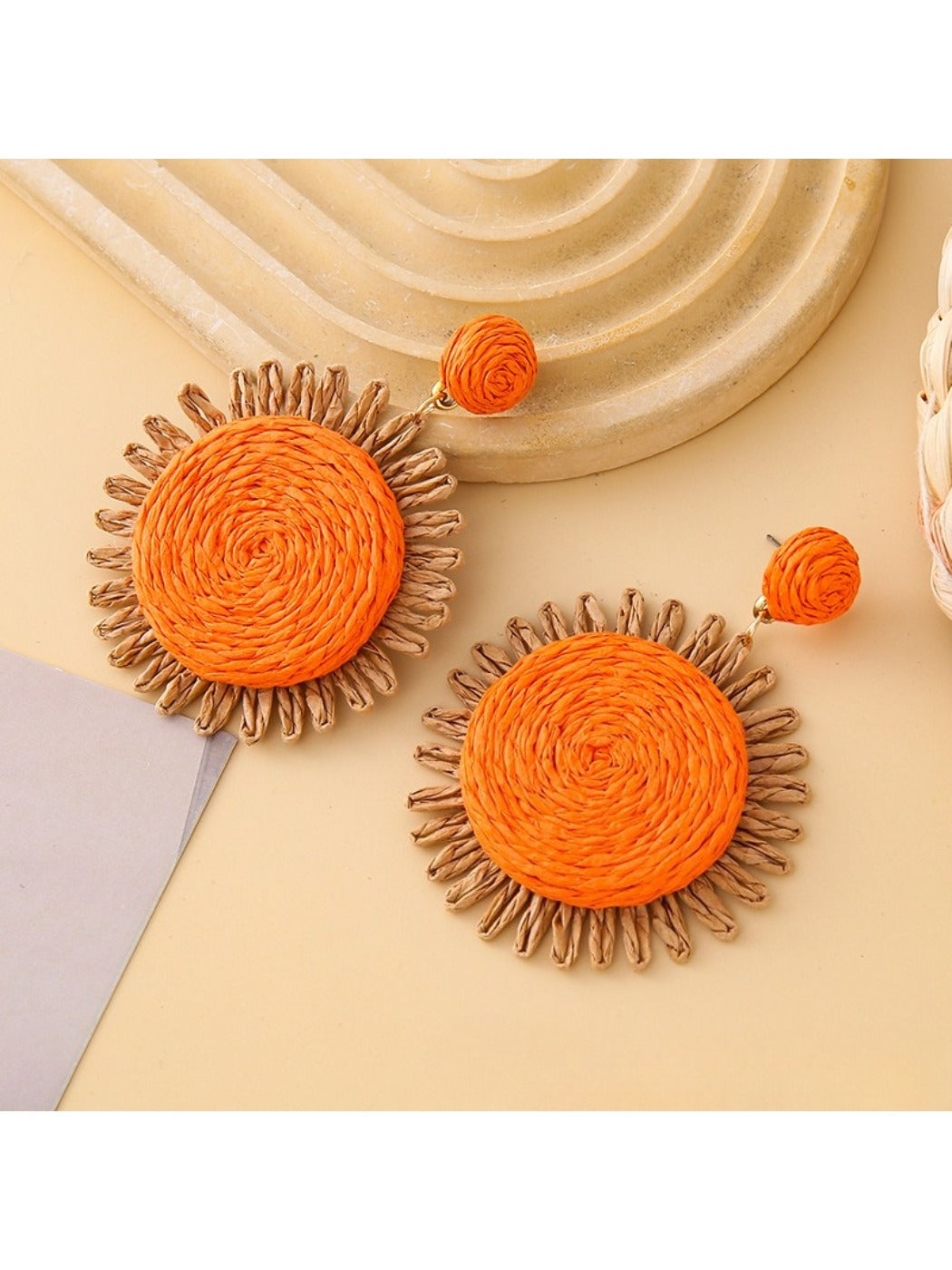Earedge raffia round earrings placed next to green leaves for styling