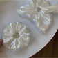 Close-up of satin white scrunchie with delicate lace trim on a white background