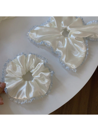 Close-up of satin white scrunchie with delicate lace trim on a white background