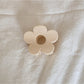 Beau flower shaped claw clip in beige next to green leaves for styling