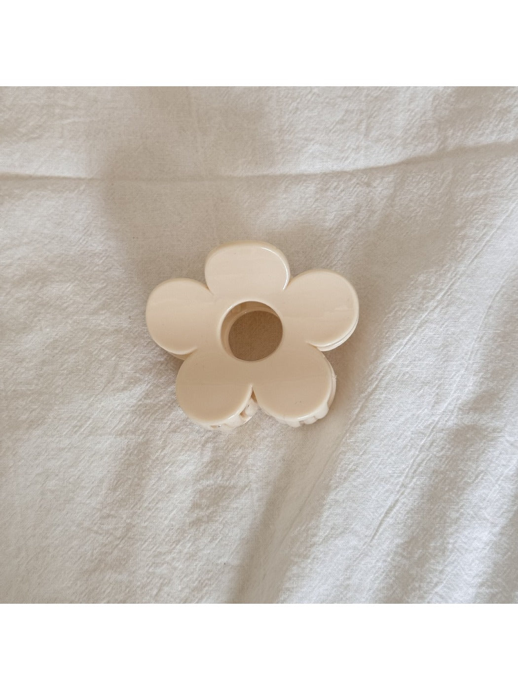 Beau flower shaped claw clip in beige next to green leaves for styling