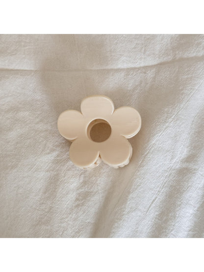Beau flower shaped claw clip in beige next to green leaves for styling