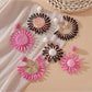 Close-up of pink and black raffia woven earring with gold-tone hoop