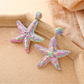 Pair of starfish raffia stud earrings placed on a light stone background
