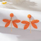 Raffia dragonfly earring held between fingers showing size