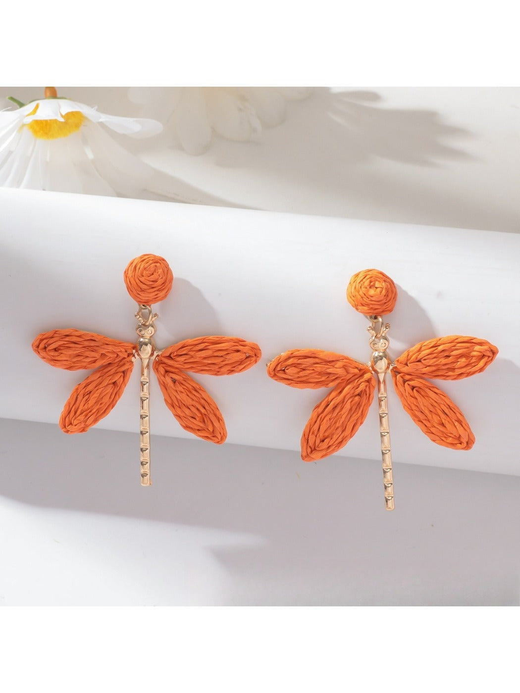 Raffia dragonfly earring held between fingers showing size