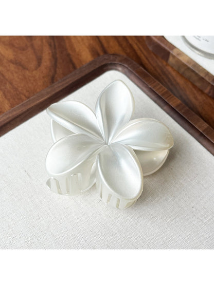 Beau flower shaped claw clip in soft pink displayed on a wooden surface