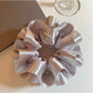 Silver satin scrunchie styled on a wrist with ruffled layers visible