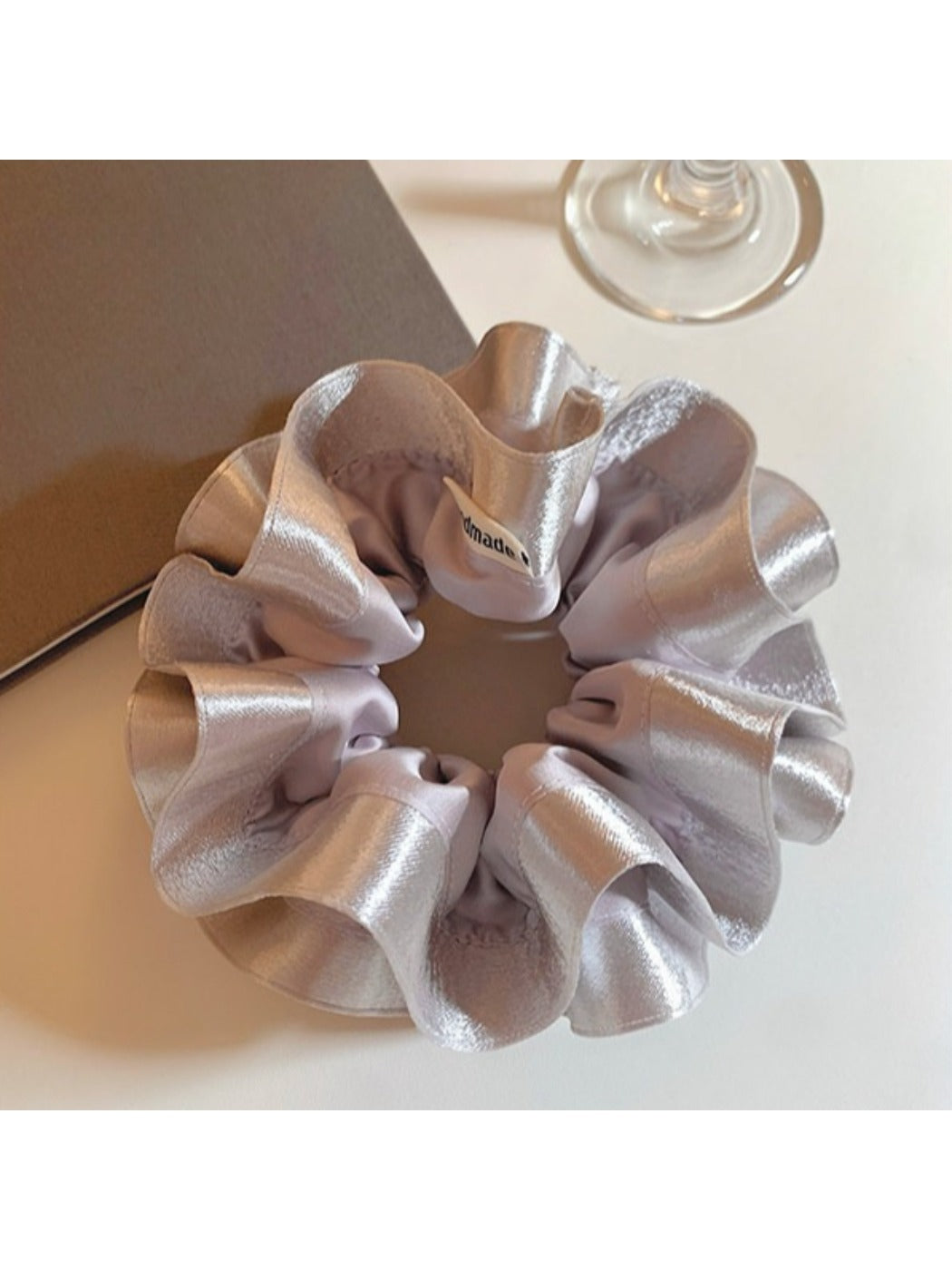 Silver satin scrunchie styled on a wrist with ruffled layers visible