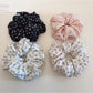 Close-up of Gifty elegant ditsy floral scrunchie with small pink and white flowers on beige fabric
