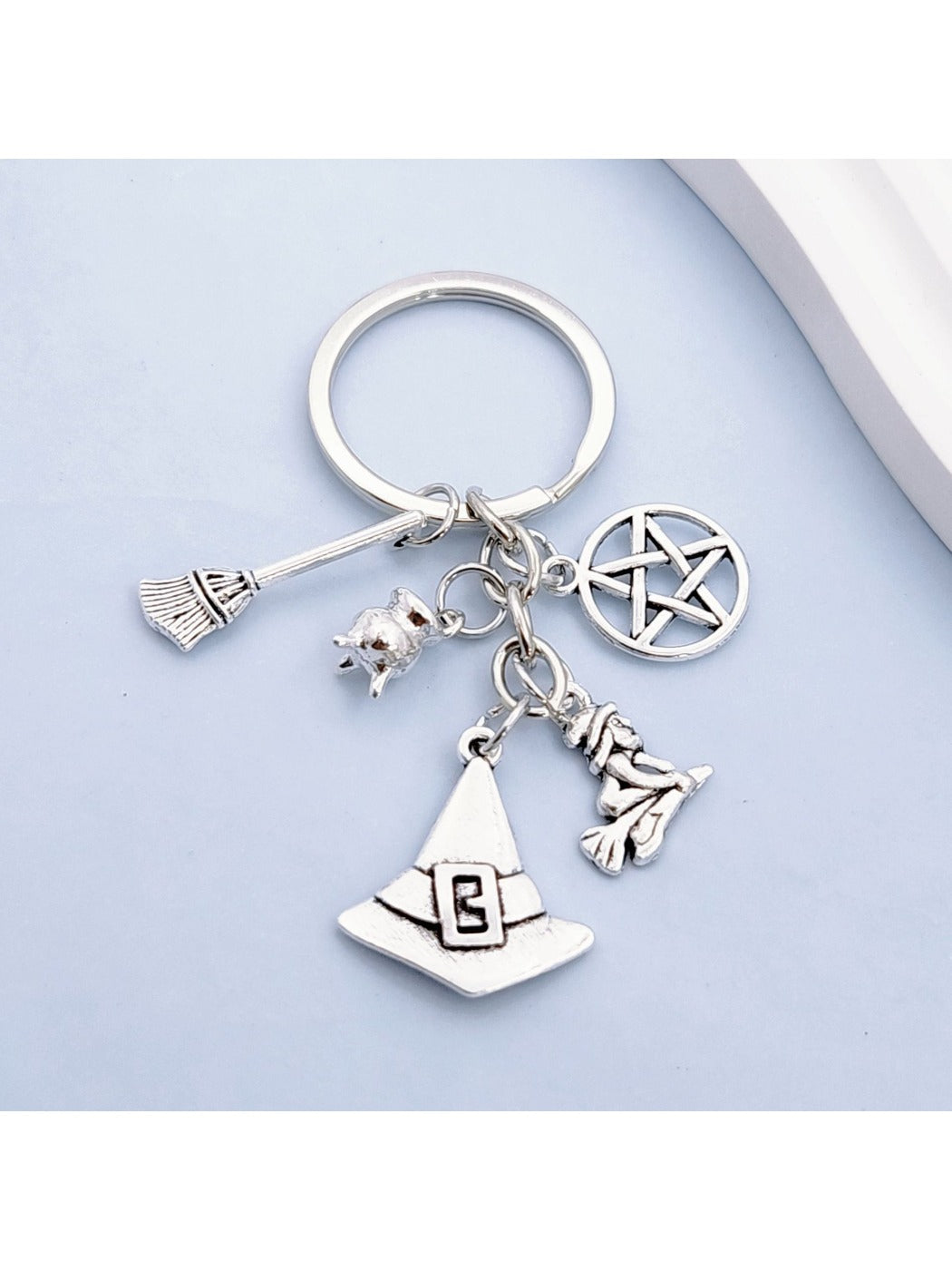 Silver witch hat and broom keychain hanging from a black cord
