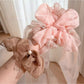 Close-up of Gifty elegant scrunchie with a large bow in soft pink fabric