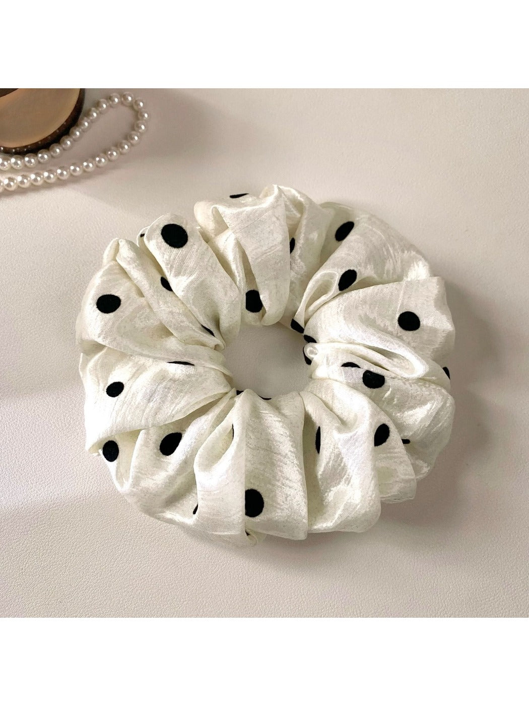 Gifty minimalist satin scrunchie with white polka dots against a soft pastel background