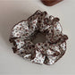 Flat lay of Gifty Retro Lace Floral Scrunchie alongside matching accessories on beige cloth