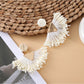 Pair of earedge fan-shaped raffia drop earrings displayed on a wooden surface