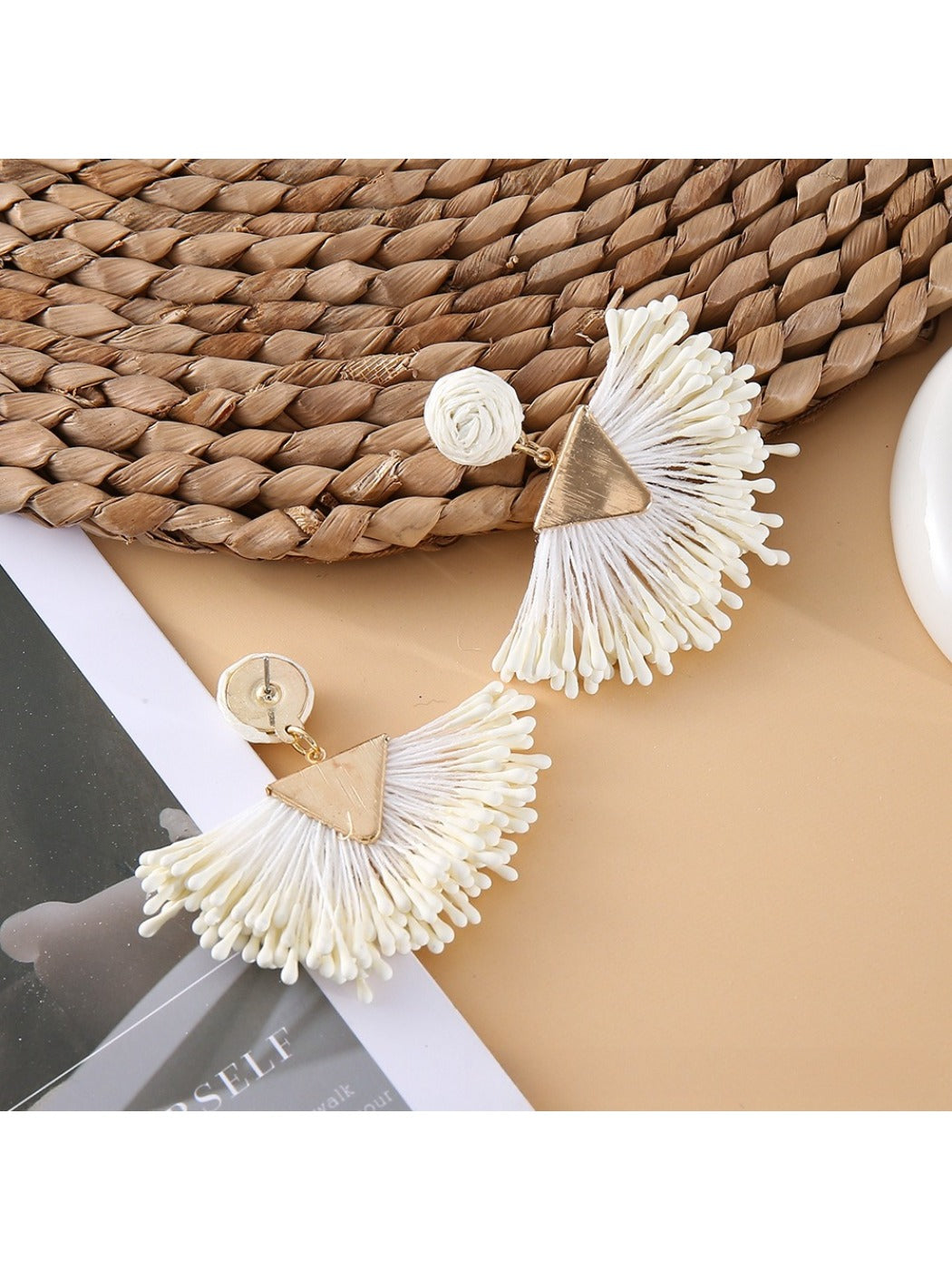 Pair of earedge fan-shaped raffia drop earrings displayed on a wooden surface
