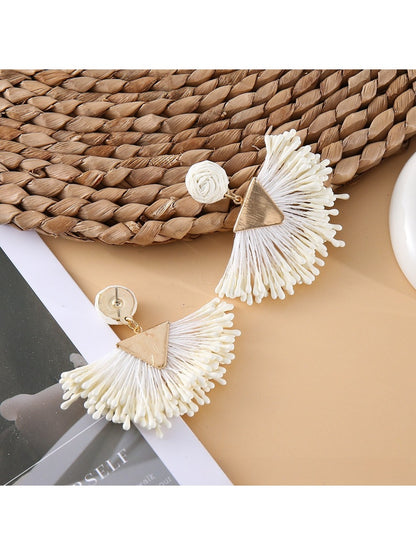 Pair of earedge fan-shaped raffia drop earrings displayed on a wooden surface