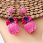 Earedge raffia ball earrings placed next to green leaves for natural aesthetic