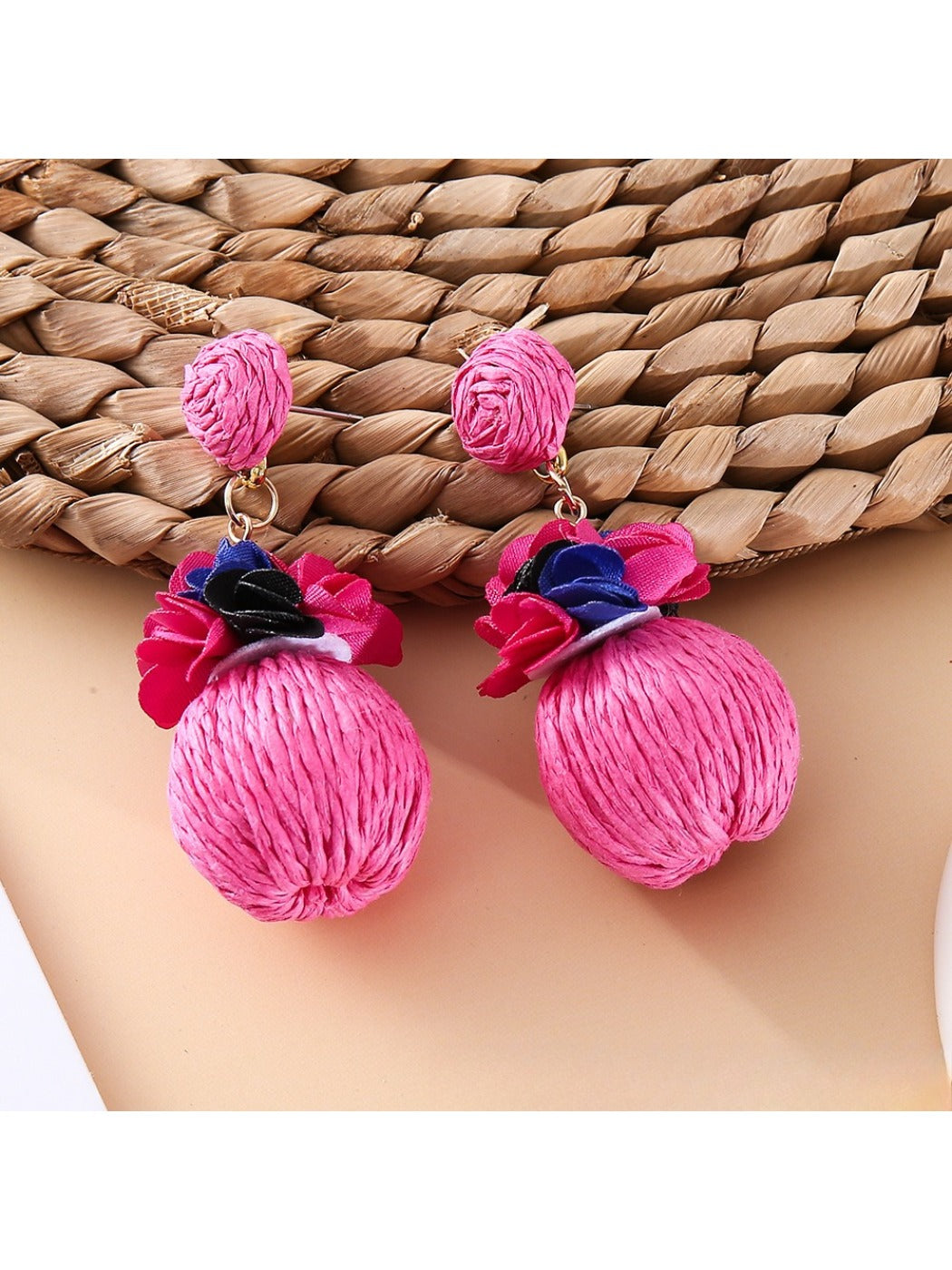 Earedge raffia ball earrings placed next to green leaves for natural aesthetic