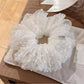 White tulle scrunchie with white polka dots on a plain background