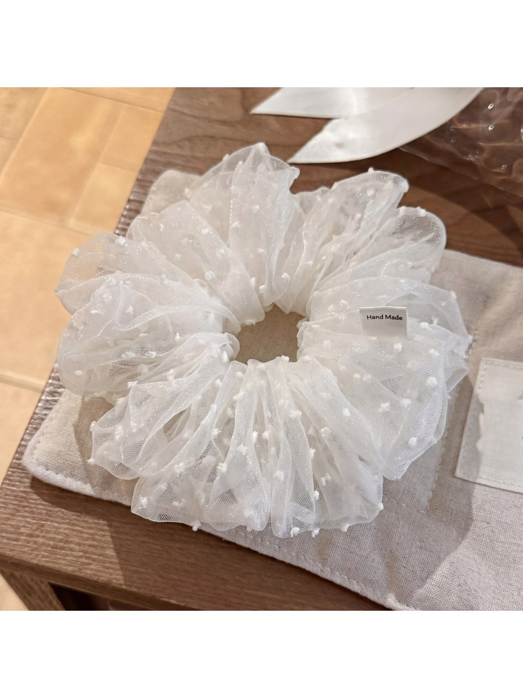 White tulle scrunchie with white polka dots on a plain background