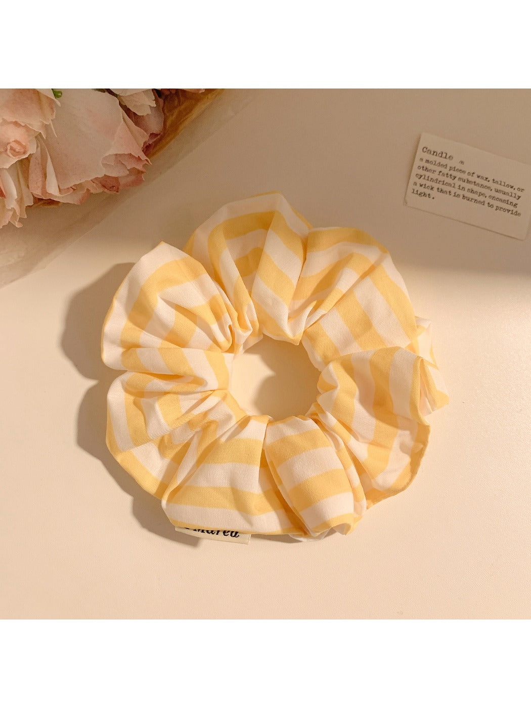 Hand holding yellow striped scrunchie against a neutral background