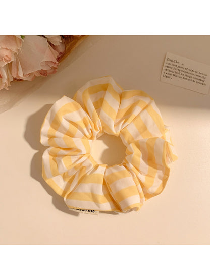 Hand holding yellow striped scrunchie against a neutral background
