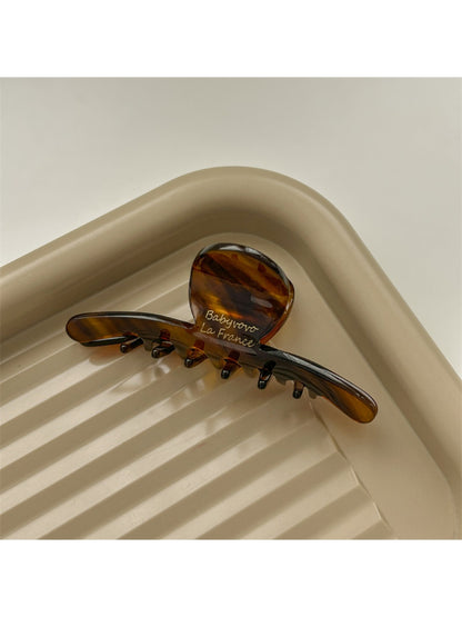 Beau brown acetate claw clip placed on wooden surface with natural light