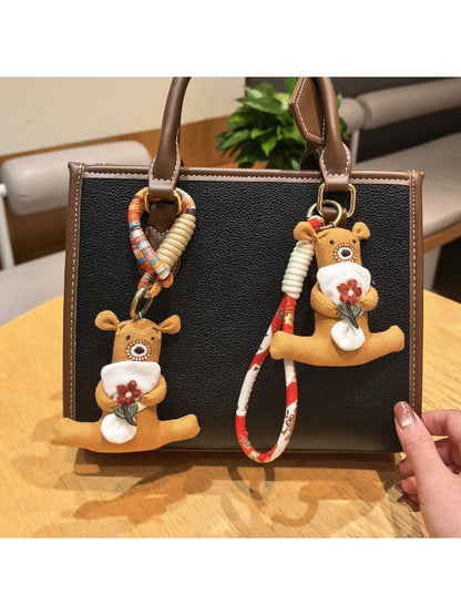 Close-up of a brown bear keychain holding a pink flower with a gold keyring